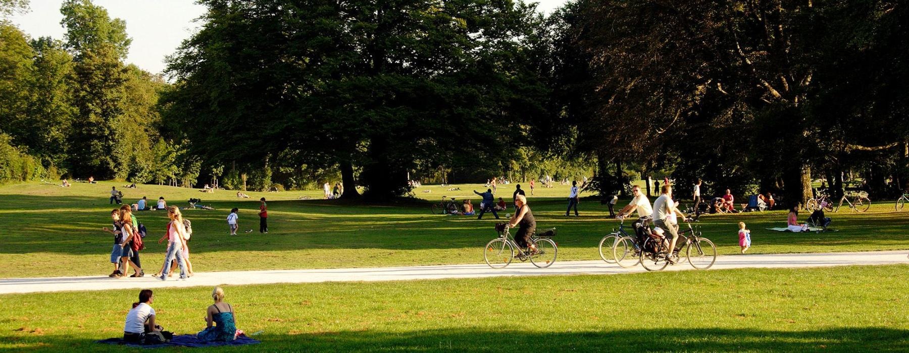 A park with many people riding bikes, having a picnic, and walking.